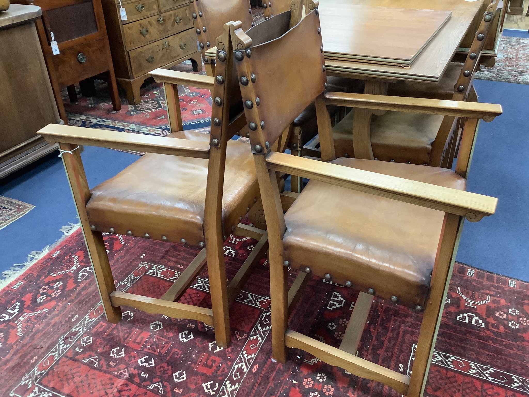 A Maple & Co oak dining suite of Italianate design, with carved and painted decoration and heraldic panels, comprising refectory table, six studded hide-covered chairs, sideboard, two-door cabinet on stand and a side tab